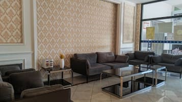 A hotel lobby with a patterned wallpaper, leather sofas, a glass coffee table, and a large window.