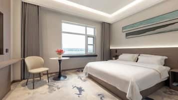 A hotel room with a bed, a chair, a small table with a vase, a window with a view, and a painting on the wall.