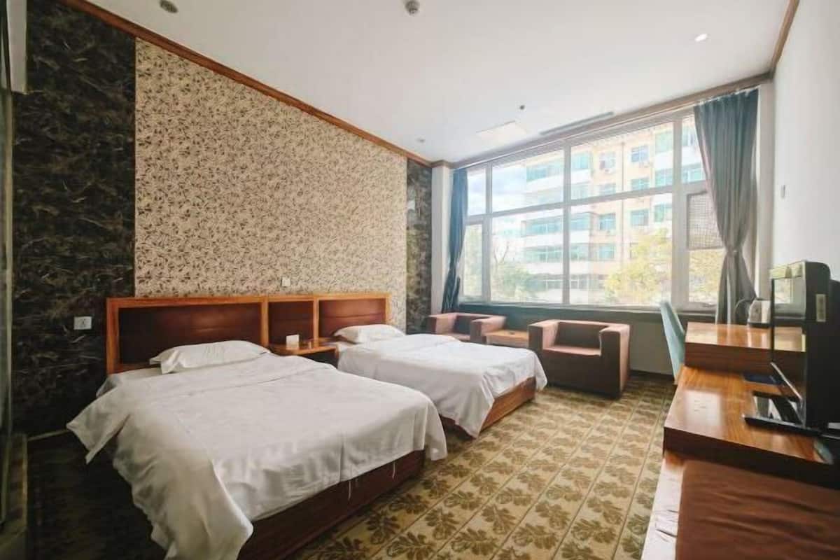 Habitación de hotel con dos camas, un escritorio, una silla y un ventanal grande.