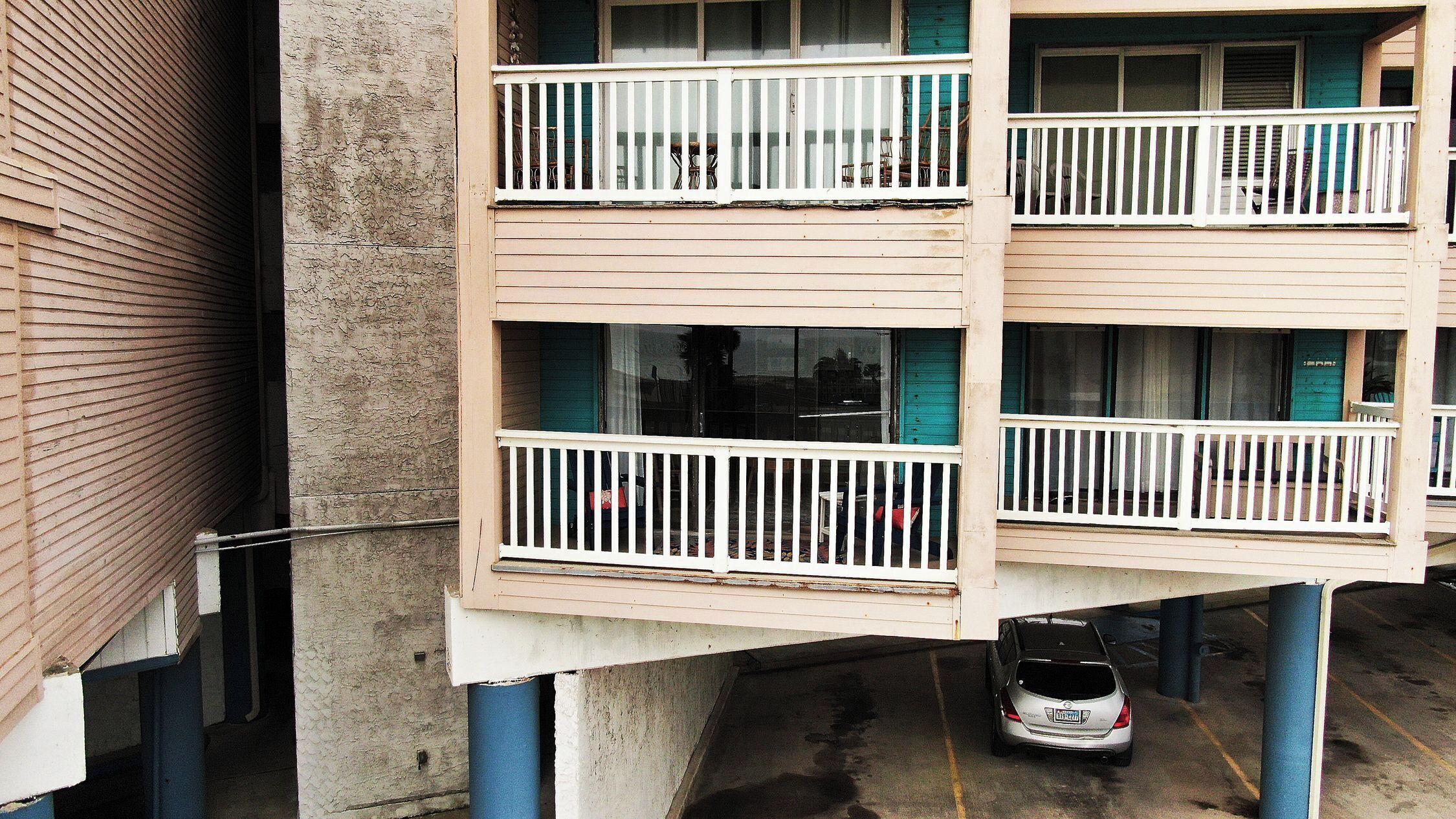 Un immeuble à plusieurs étages doté de balcons, avec une voiture garée en contrebas et une porte bien visible.