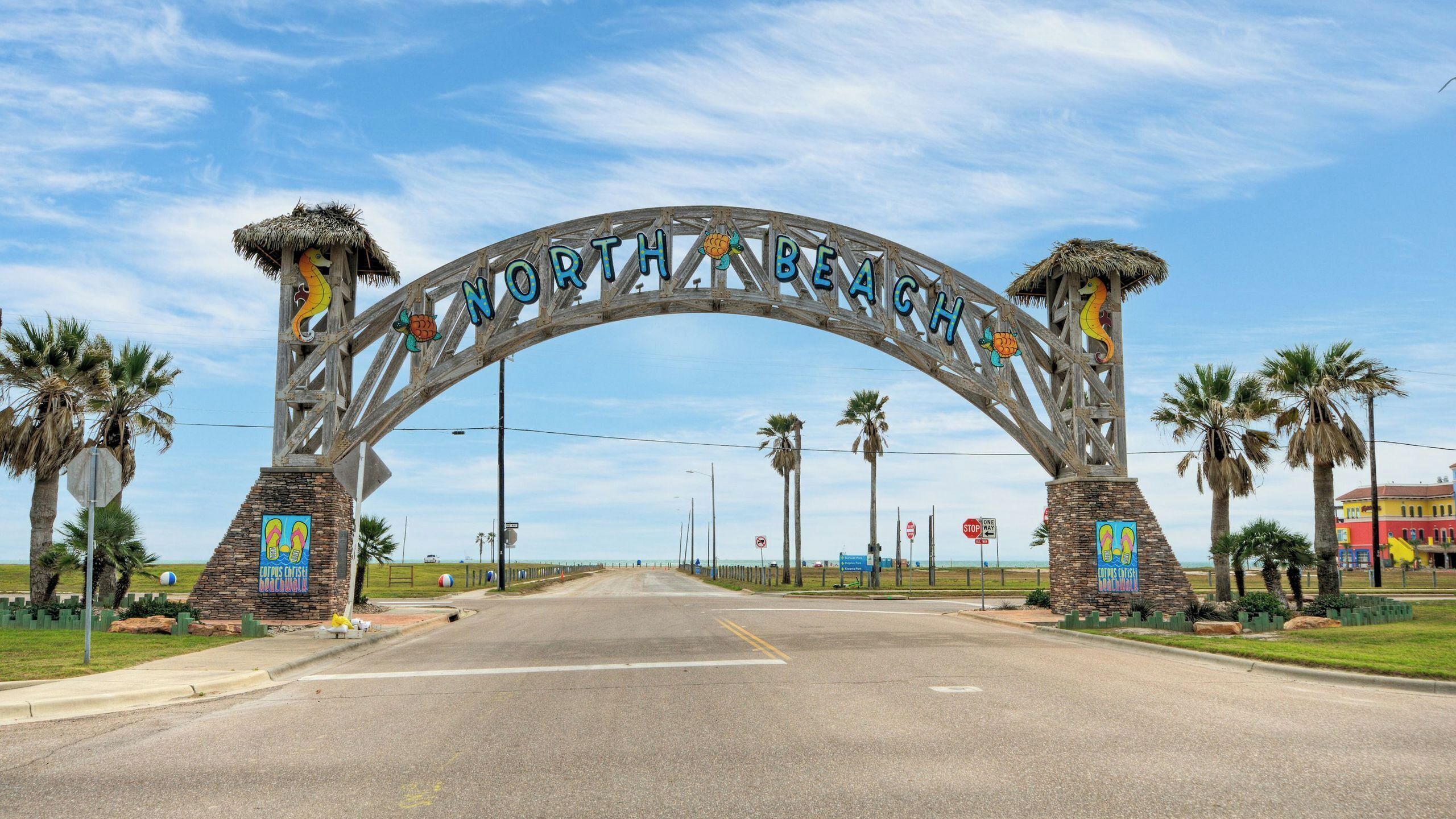 A road leading to a sign with 'North Beach' written on it, flanked by palm trees and a clear sky.