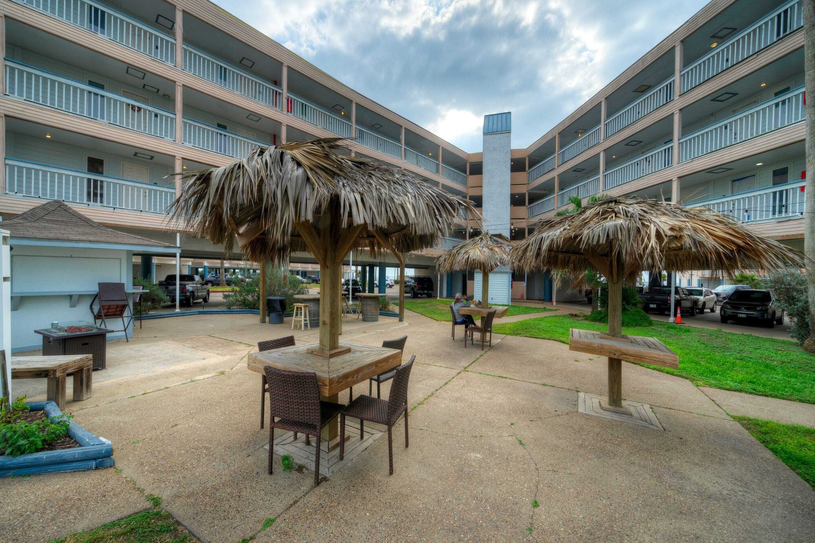 Un patio con mobiliario exterior, piscina y un edificio de varios pisos con balcones.