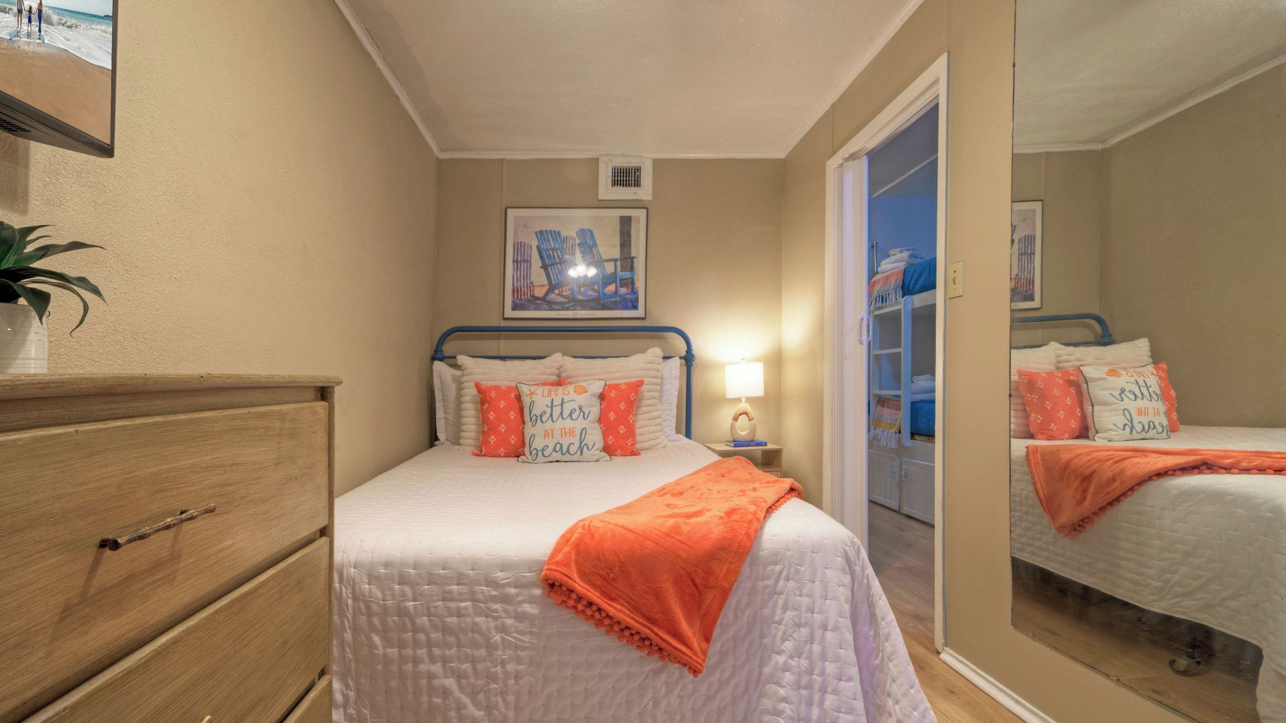Una camera da letto con un letto, una cassettiera, un comodino, una lampada, un quadro appeso e uno specchio.