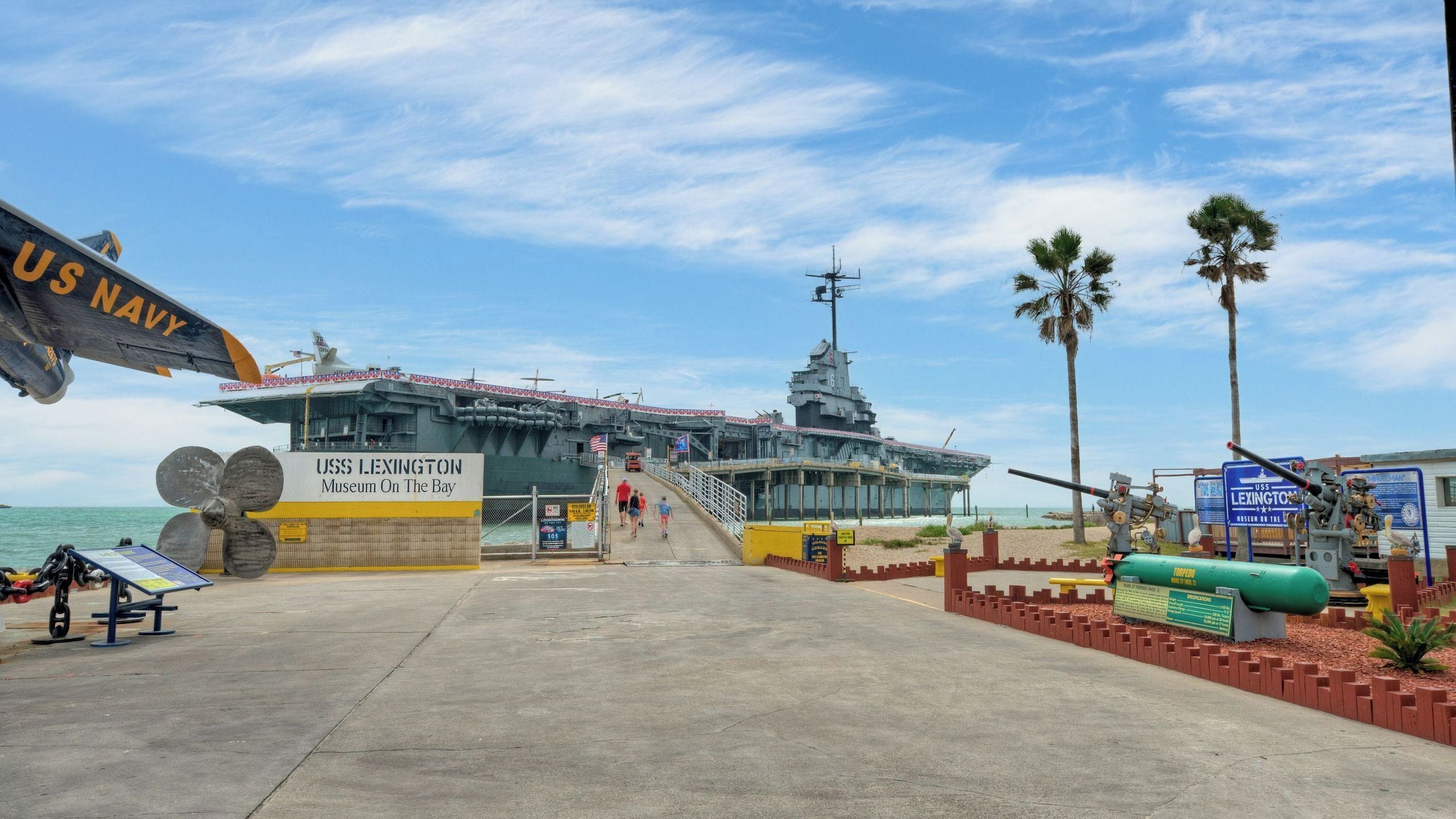 Ein US Navy Schiff, die USS Lexington, liegt an einem Museum in einer Bucht unter einem klaren Himmel vor Anker.