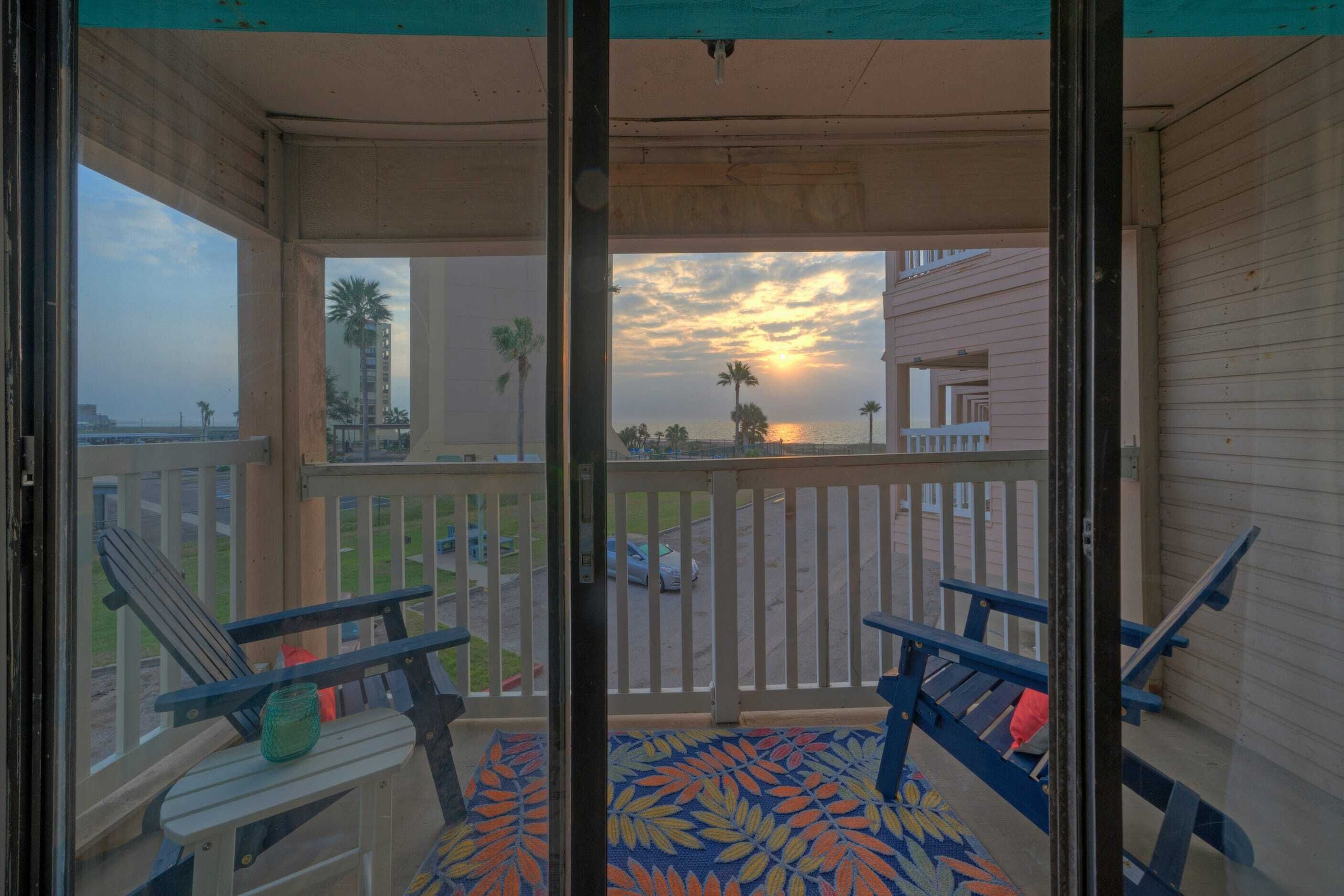 A balcony with a view of the sunset, wooden railings, and a patterned floor.