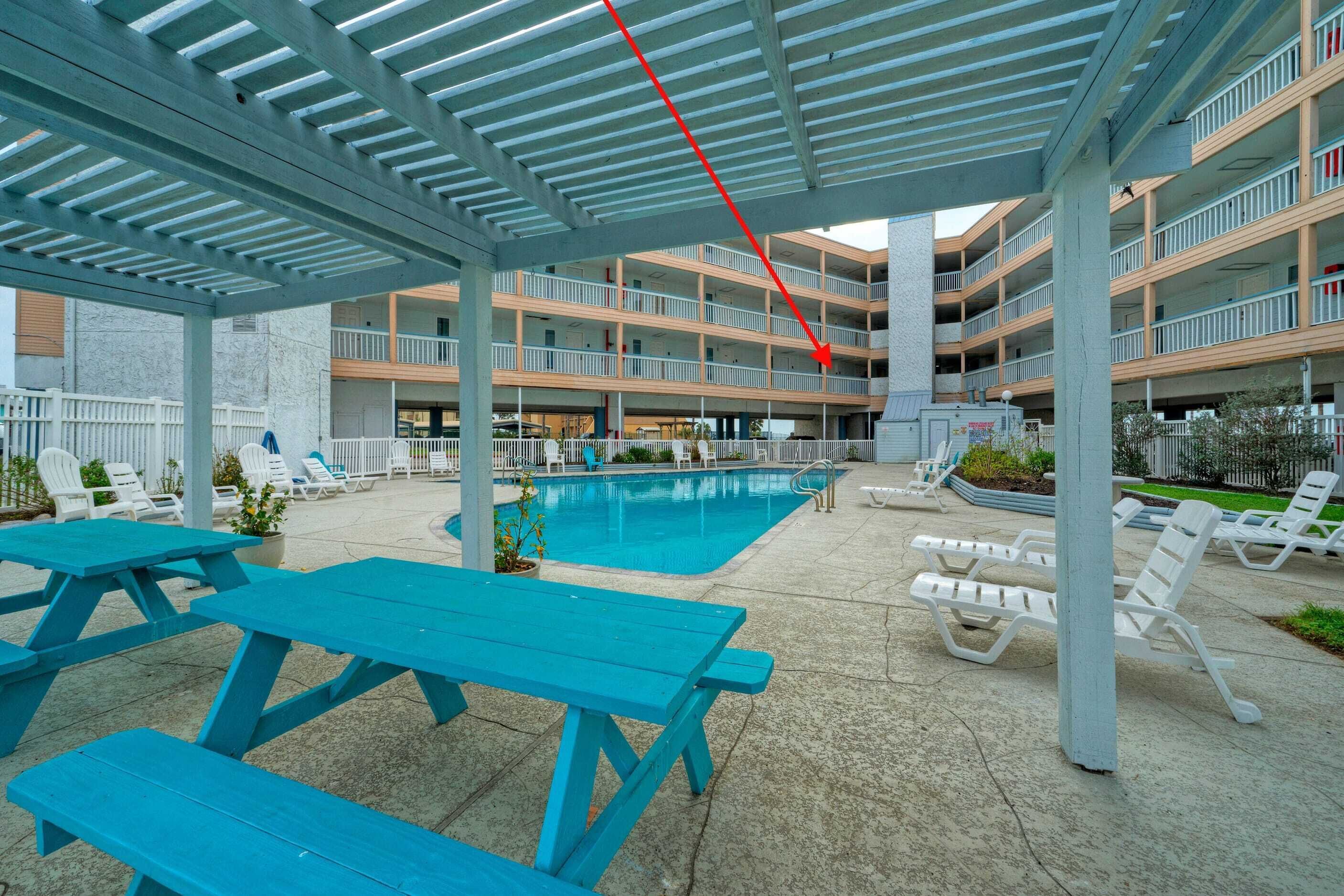 Un espace piscine extérieur abrité, avec des tables de pique-nique bleues et des chaises longues blanches.