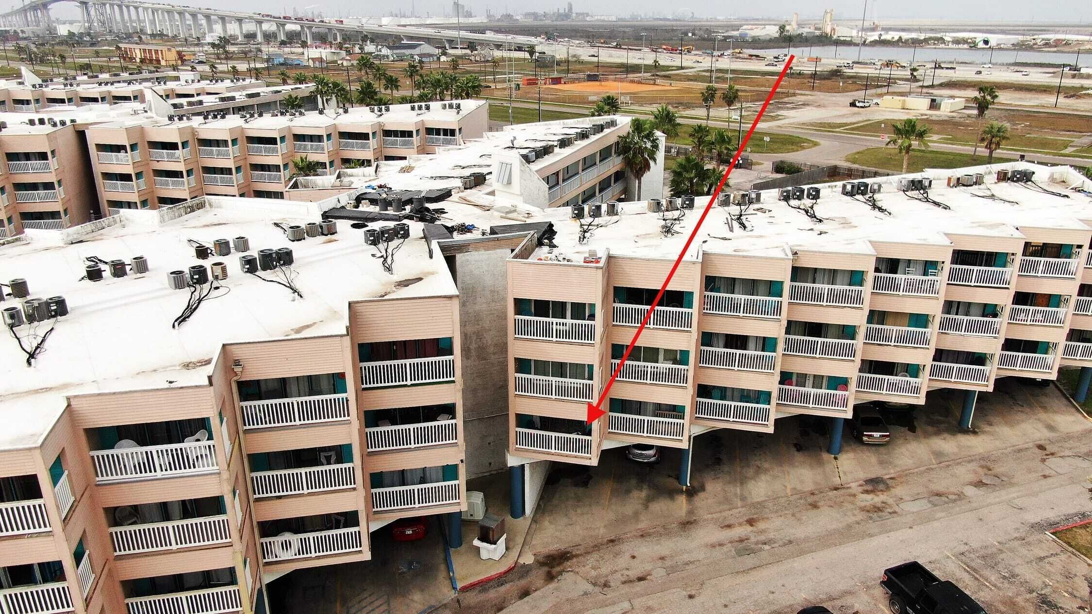 Un hotel de varios pisos con terraza en la azotea, unidades de aire acondicionado y vistas del entorno, incluyendo un puente y una masa de agua.