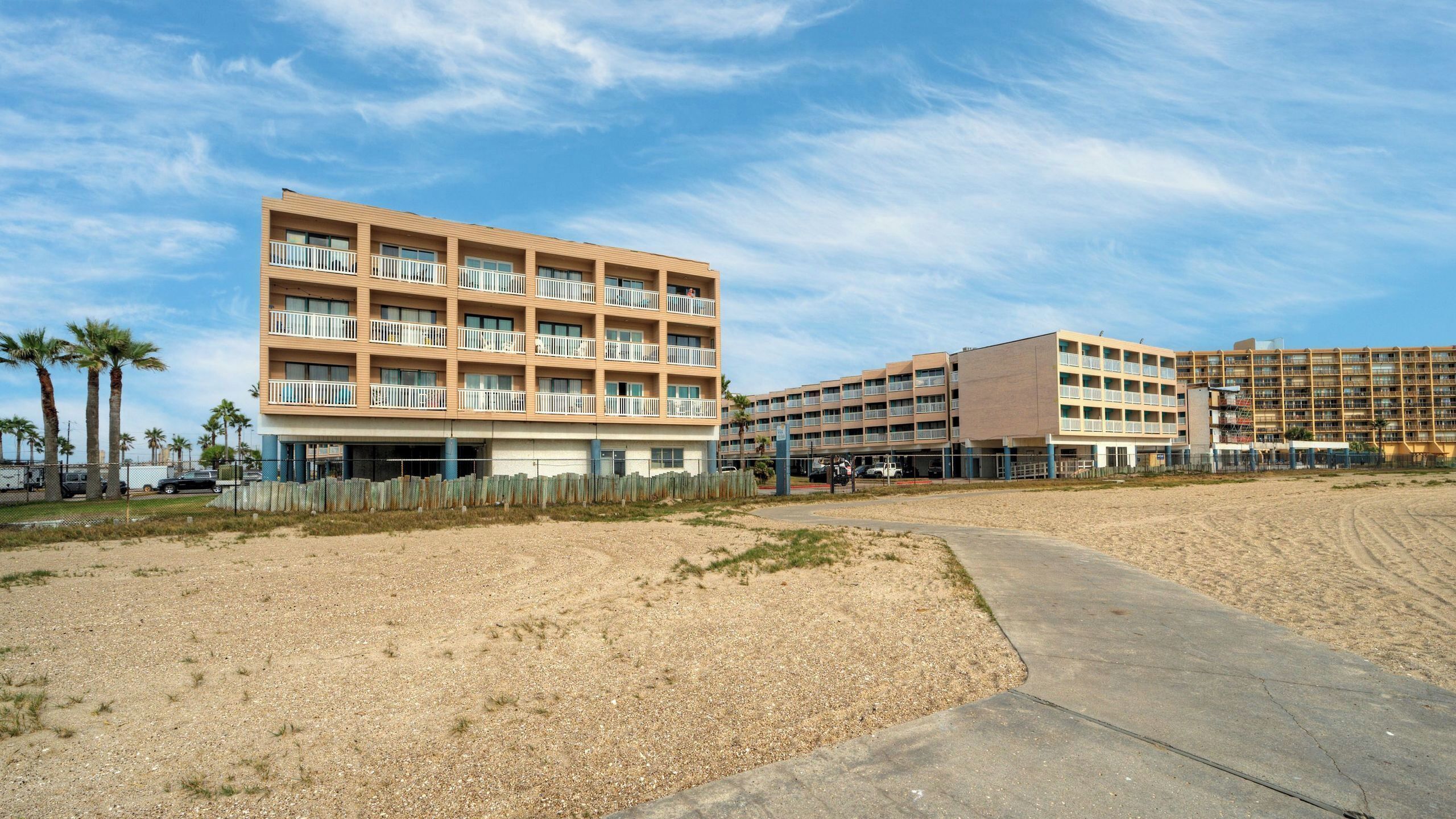 A beachfront hotel with multiple balconies, a parking area, and a sandy beach.