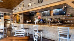 Eine Bar mit Backsteinwand, Holzbalkendecke und verschiedenen Sitzgelegenheiten.
