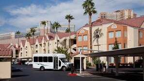 Ein Hotel mit überdachter Bushaltestelle, Palmen und einem Parkplatz.