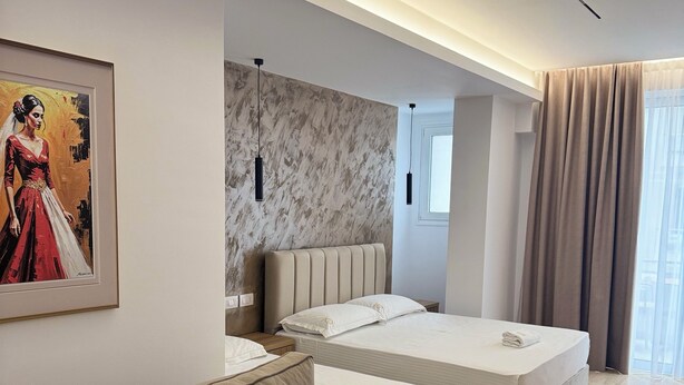 A modern hotel room with a large bed, a sofa, a painting, and a marble wall. - Hotel Moonlight (Vlorë)