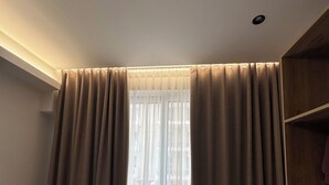 A room with a large window covered by beige curtains, a wooden floor, and a ceiling light. - Hotel Moonlight (Vlorë)