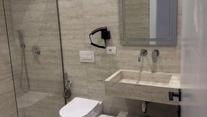 A modern bathroom with a glass-enclosed shower, a white toilet, a sink with a mirror, and a trash bin. - Hotel Moonlight (Vlorë)