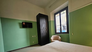 Une pièce aux murs verts, avec un lit, une armoire noire, une chaise et une fenêtre.