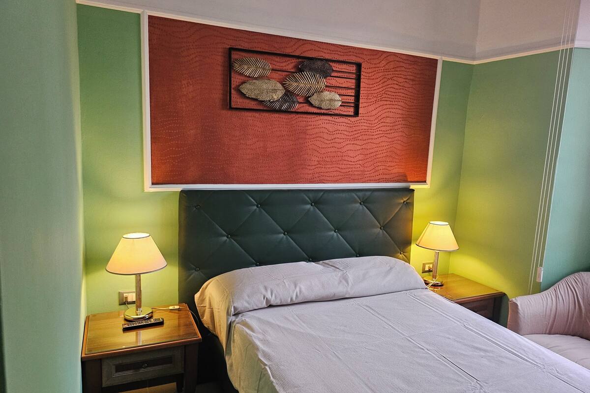 A hotel room with a bed, two bedside tables with lamps, a decorative wall panel, and a green wall.