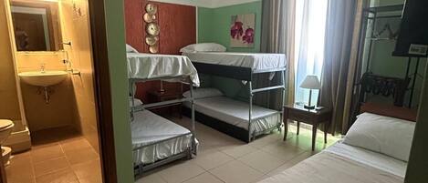 Une chambre d’hôtel avec une salle de bain, deux lits superposés, un lit simple, une chaise et un bureau.