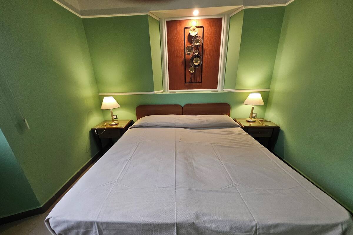 A single bed in a room with green walls, two bedside tables with lamps, and a wall decoration above the bed.