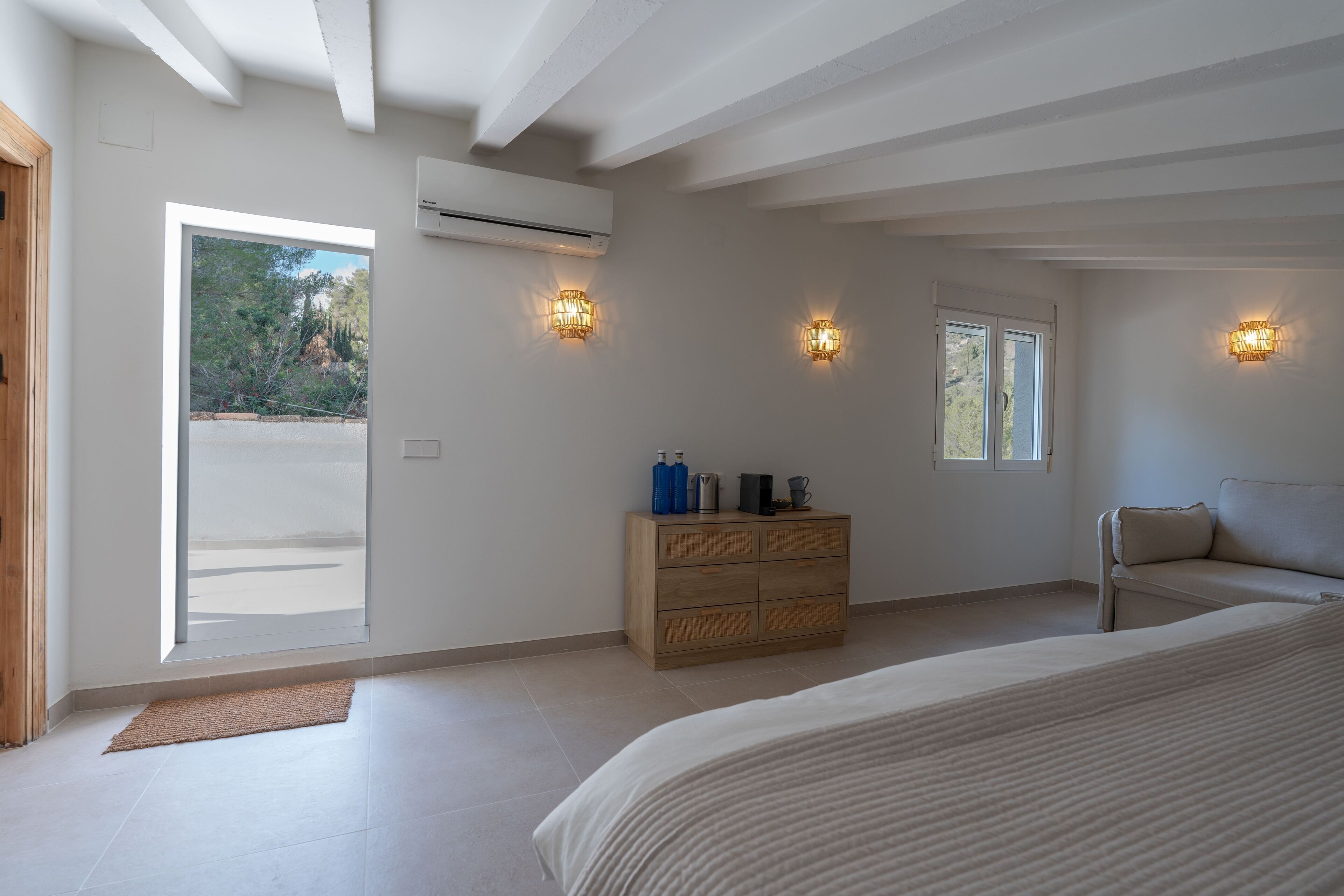 A bedroom with a bed, a wooden dresser, and two wall-mounted lights.