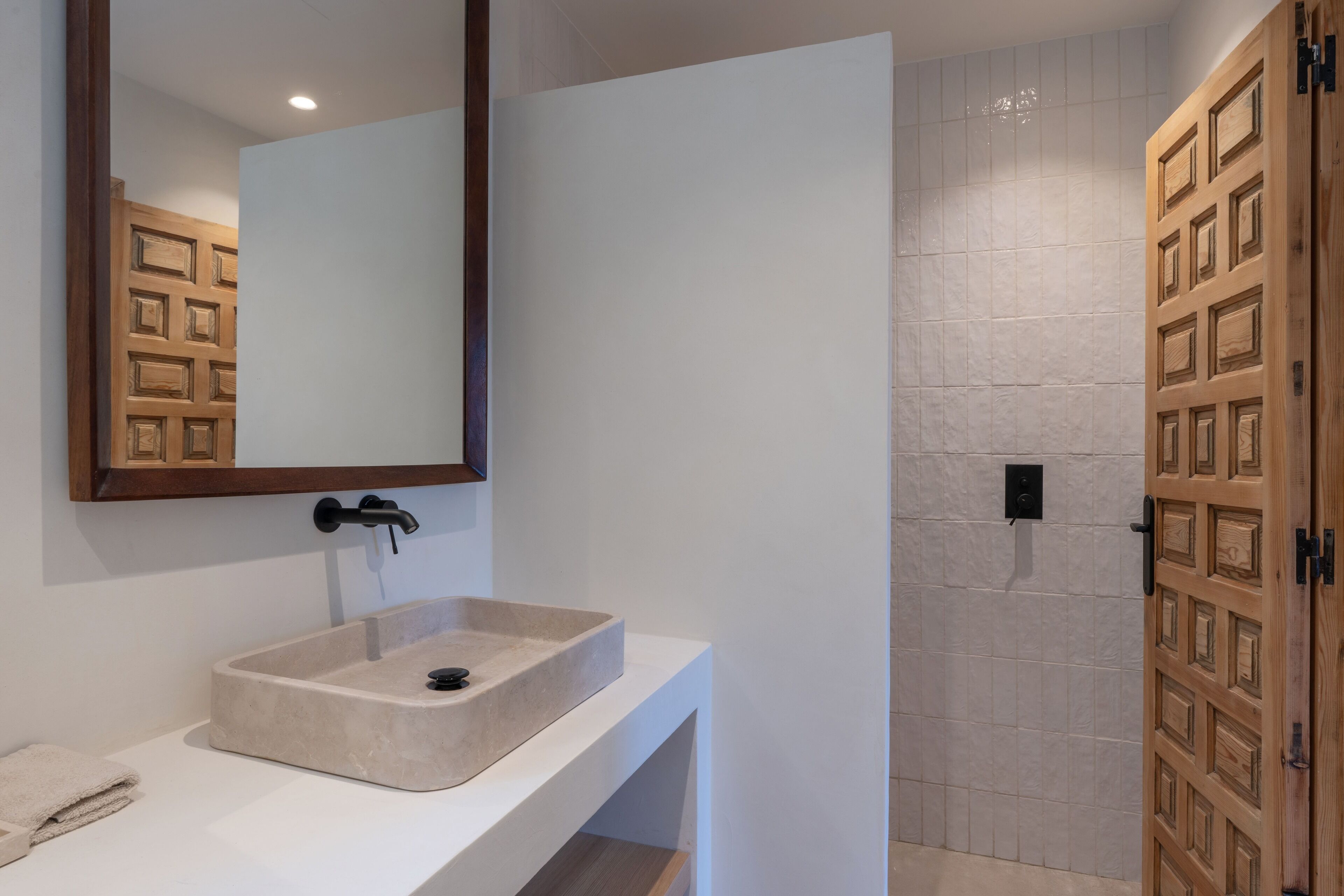Une salle de bain avec un lavabo beige, un miroir et un espace douche doté d’une porte en bois.