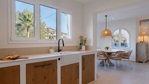A modern kitchen with a large window, wooden cabinets, and a dining area with wicker chairs.