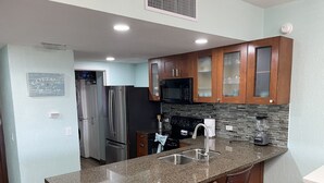 A modern kitchen with granite countertops, stainless steel appliances, and wooden cabinets. - RockyCondo - Princesa A-407 Beach Front 2 Bed 2 Bath Condo (Puerto Penasco)