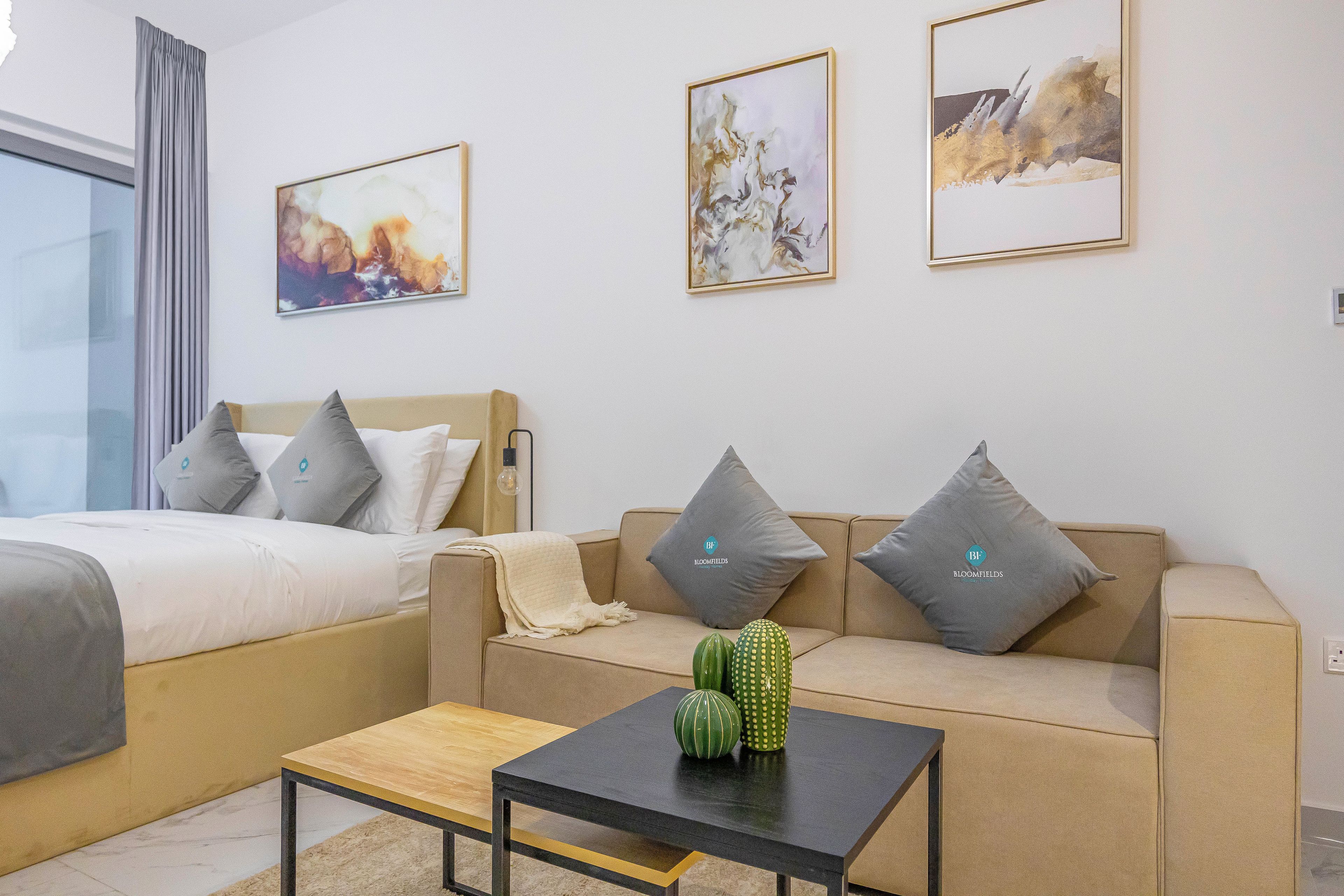 A hotel room with a bed, a sofa, a coffee table, and three framed artworks on the wall.