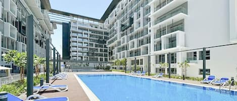 Un hotel moderno con piscina, tumbonas y vistas a la arquitectura del edificio.