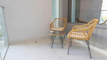 A balcony with two wicker chairs and a small round table, a glass railing, and a view of the outside.