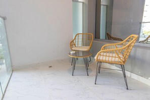 A balcony with two wicker chairs and a small round table, a glass railing, and a view of the outside. - Bloomfields Fantastic STU in Oasis (Abu Dhabi)