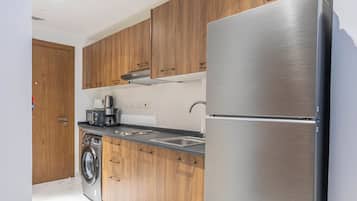 A modern kitchen with wooden cabinets, a stainless steel refrigerator, a built-in washing machine, and a coffee maker.