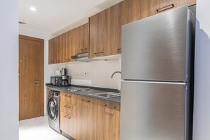 A modern kitchen with wooden cabinets, a stainless steel refrigerator, a built-in washing machine, and a coffee maker. - Bloomfields Fantastic STU in Oasis (Abu Dhabi)