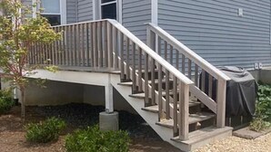 A wooden staircase leading to a deck with a railing, surrounded by gravel and small plants. - Walk to Beach & Festivities All Summer at the Jersey Shore! (Long Branch)