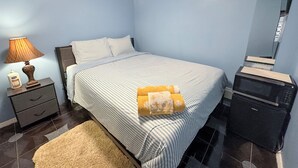 Une chambre à coucher avec un lit, une table de chevet, une lampe, une bouteille de lotion, une serviette, une commode et un miroir.