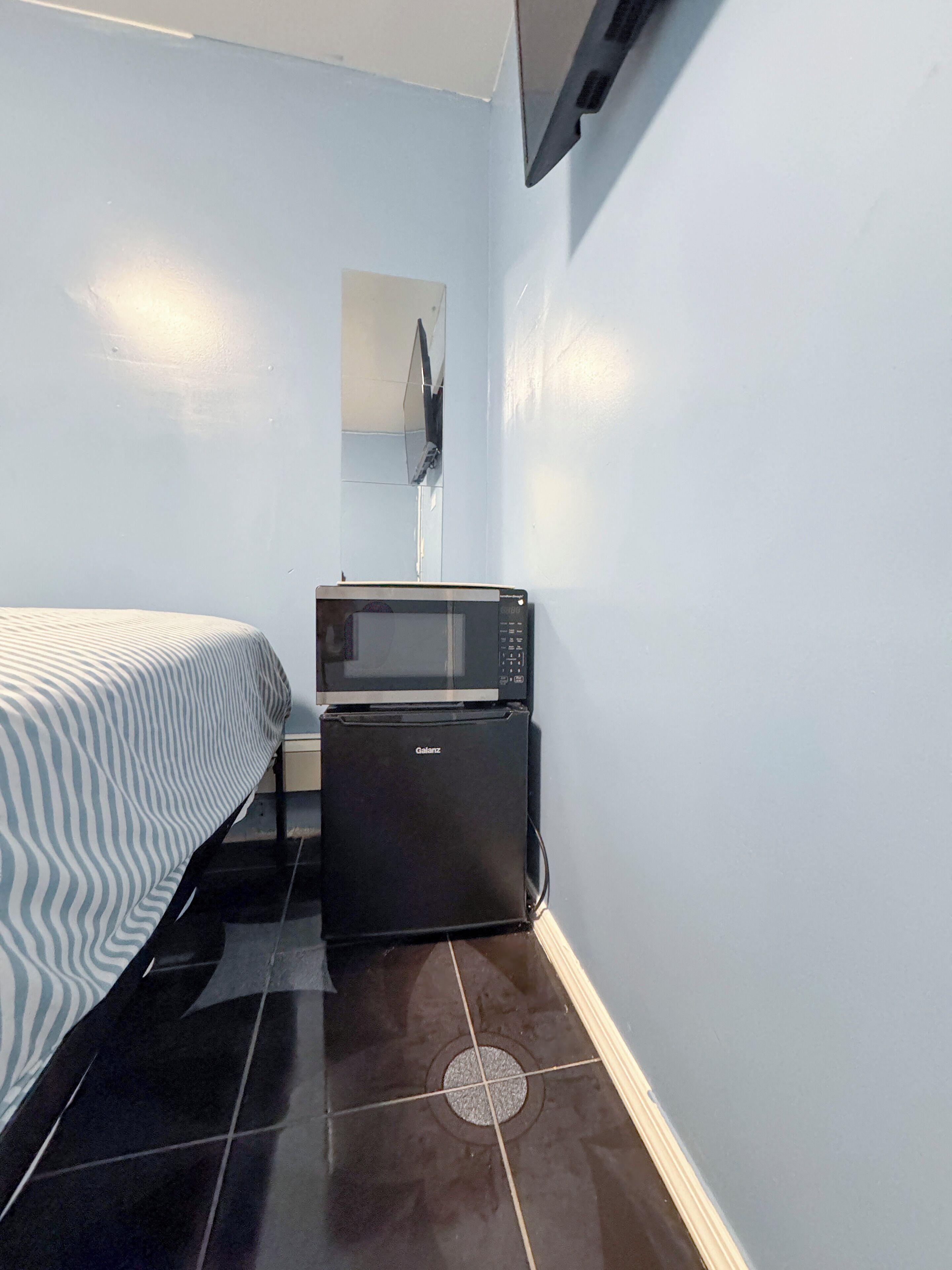 Una habitación pequeña y funcional con cama, microondas y refrigerador.