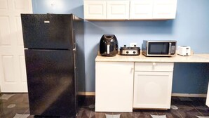 Une cuisine compacte avec un réfrigérateur noir, une machine à café, un four à micro-ondes et un grille-pain posés sur le plan de travail.