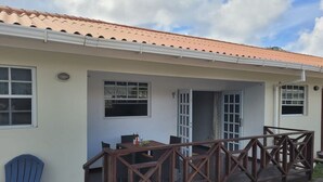A building with a tiled roof, a covered porch with a wooden railing, and a dining area with a table and chairs. - Apartment centrally located near Mambo beach Curacao (Willemstad)