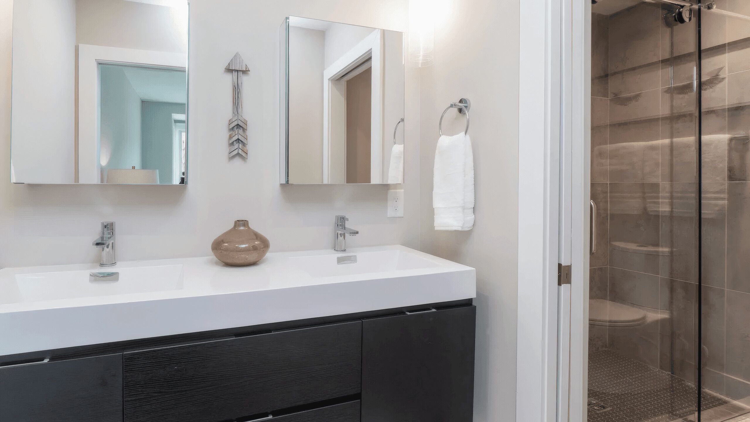 Une salle de bain avec un meuble-lavabo blanc, deux miroirs, un porte-serviettes et un espace douche.