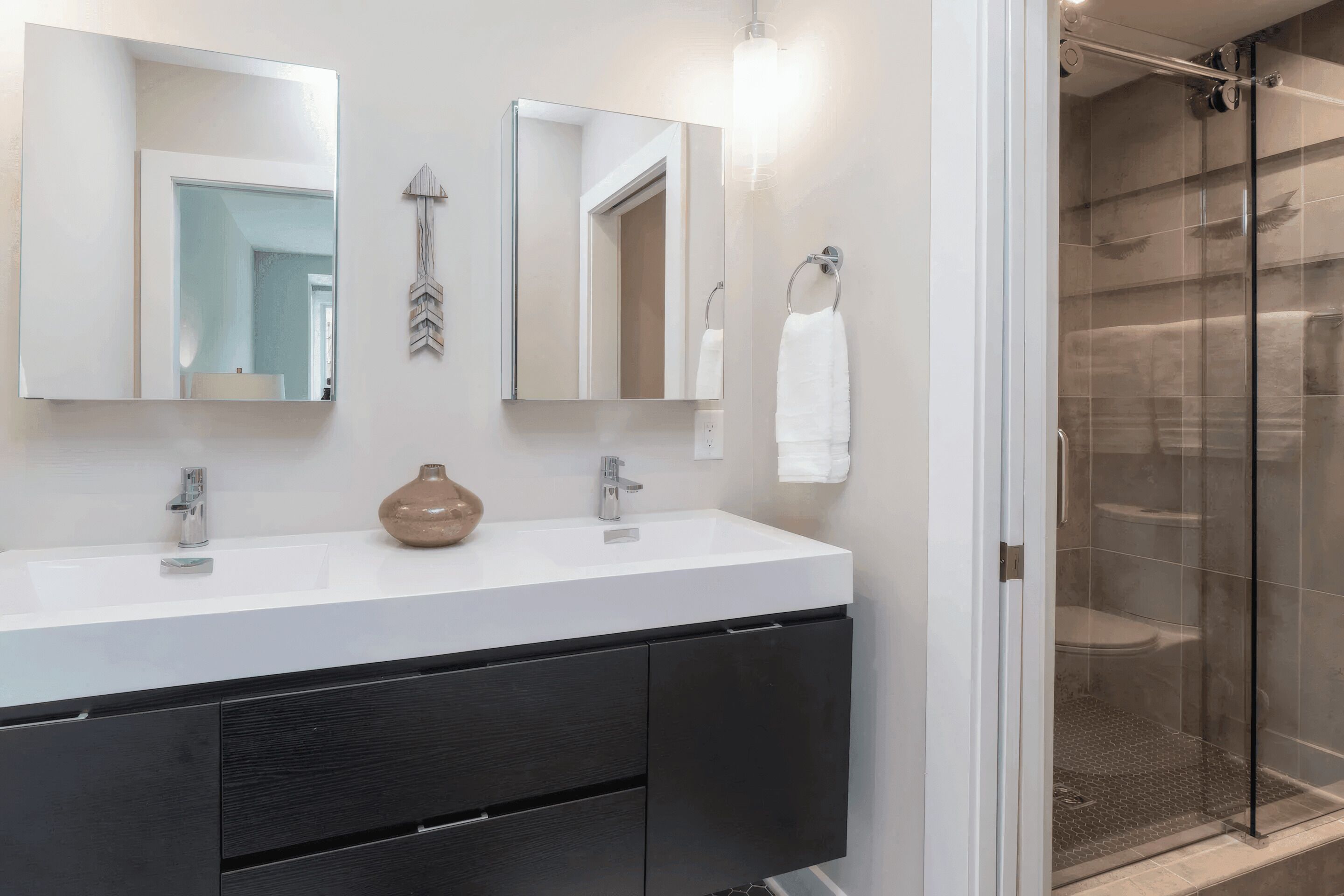 A bathroom with a white sink, two mirrors, a towel rack, and a glass shower enclosure.