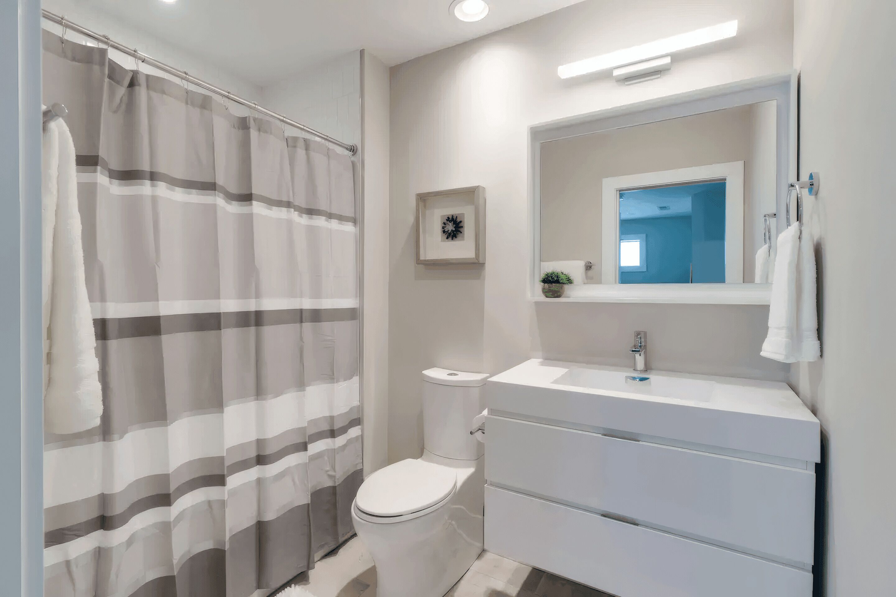 A modern bathroom with a shower curtain, toilet, sink, and mirror.