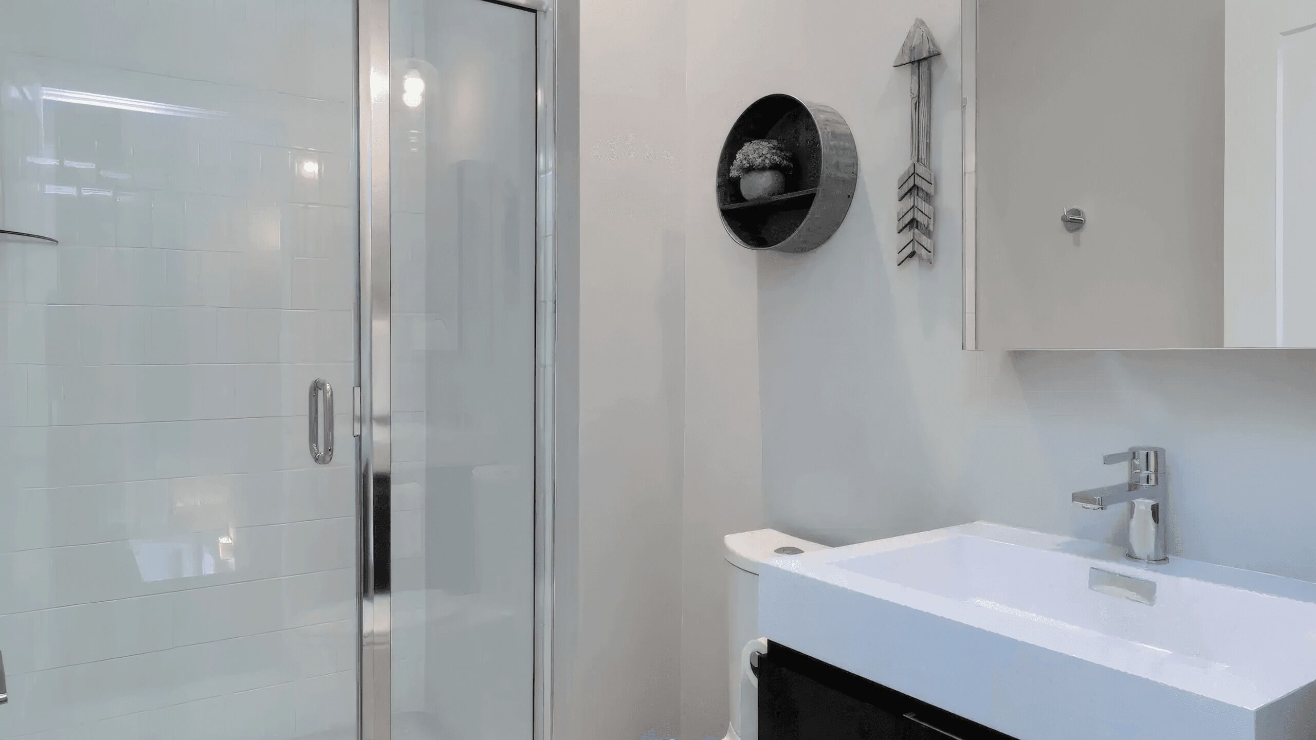 Ein modernes Badezimmer mit Duschabtrennung aus Glas, einem weißen Waschbecken und einem Spiegel darüber.