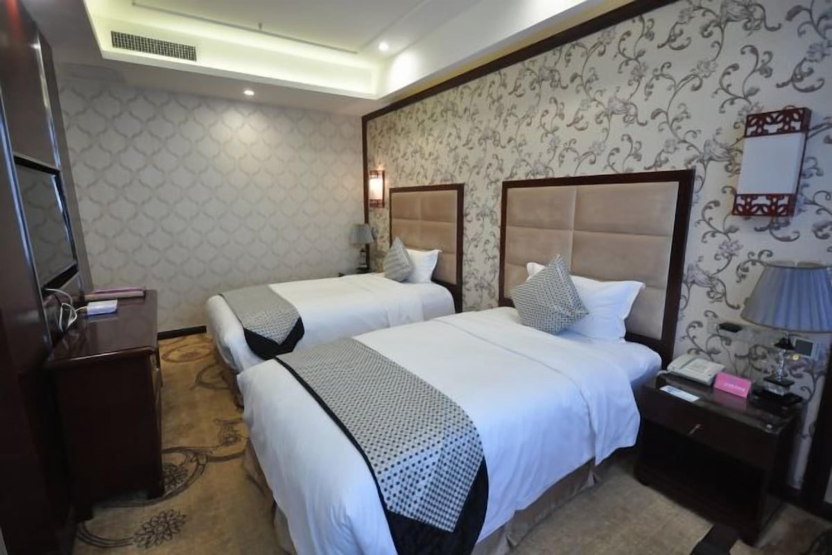 A hotel room with two beds, a desk, a chair, a TV, and a bathroom.