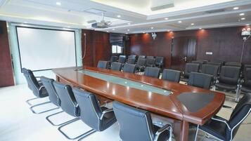 Una sala de conferencias con una larga mesa, varias sillas, una pantalla de proyector y una pizarra.
