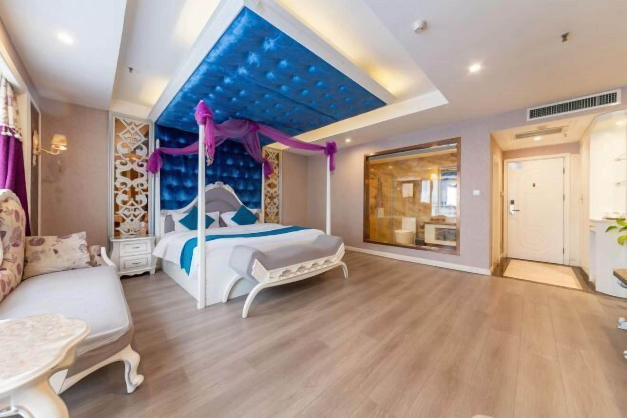 A modern bedroom with a bed, a seating area, and a large window.