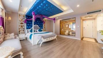 A modern bedroom with a bed, a seating area, and a large window.