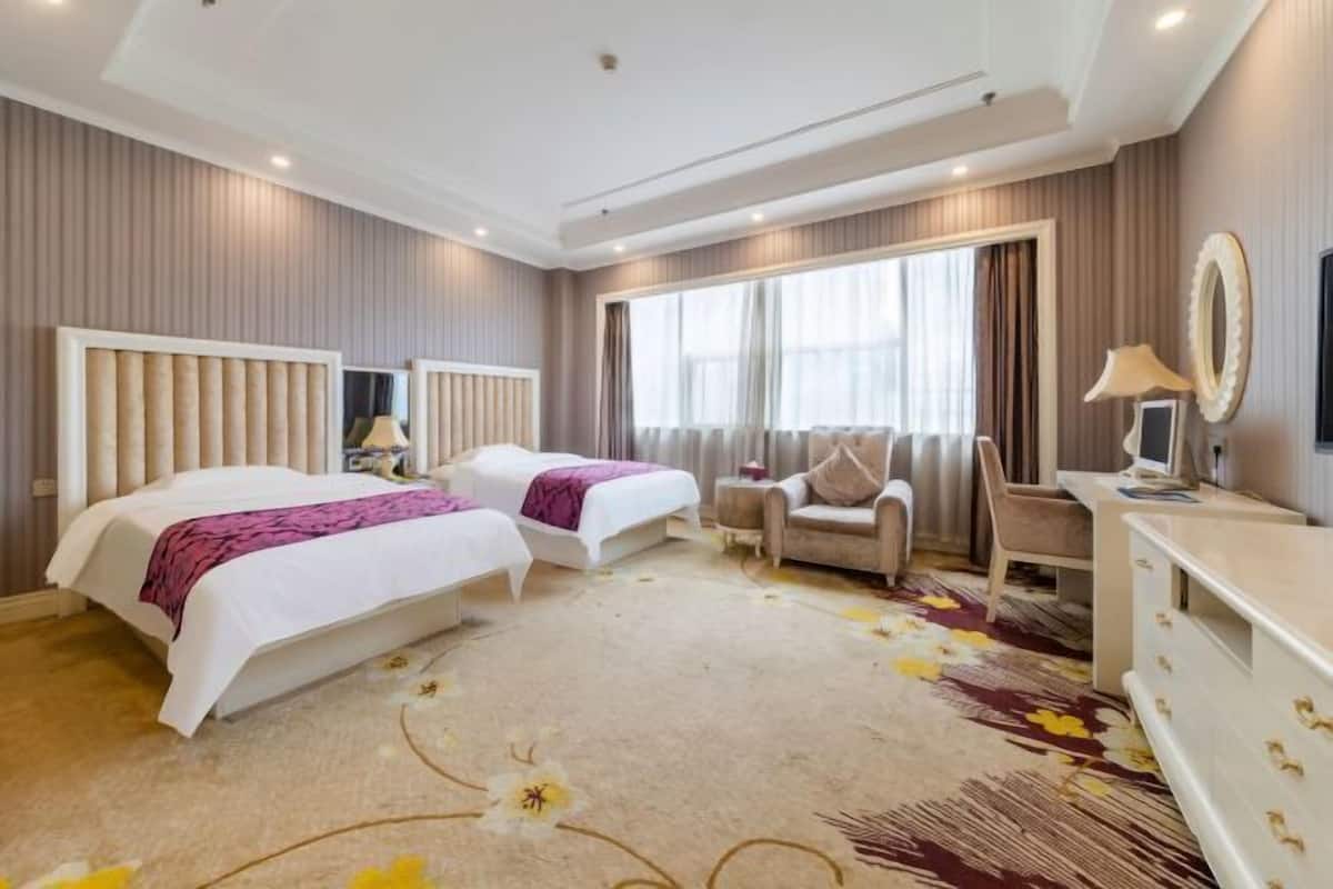 A hotel room with two beds, a sofa, a desk, and a large window.
