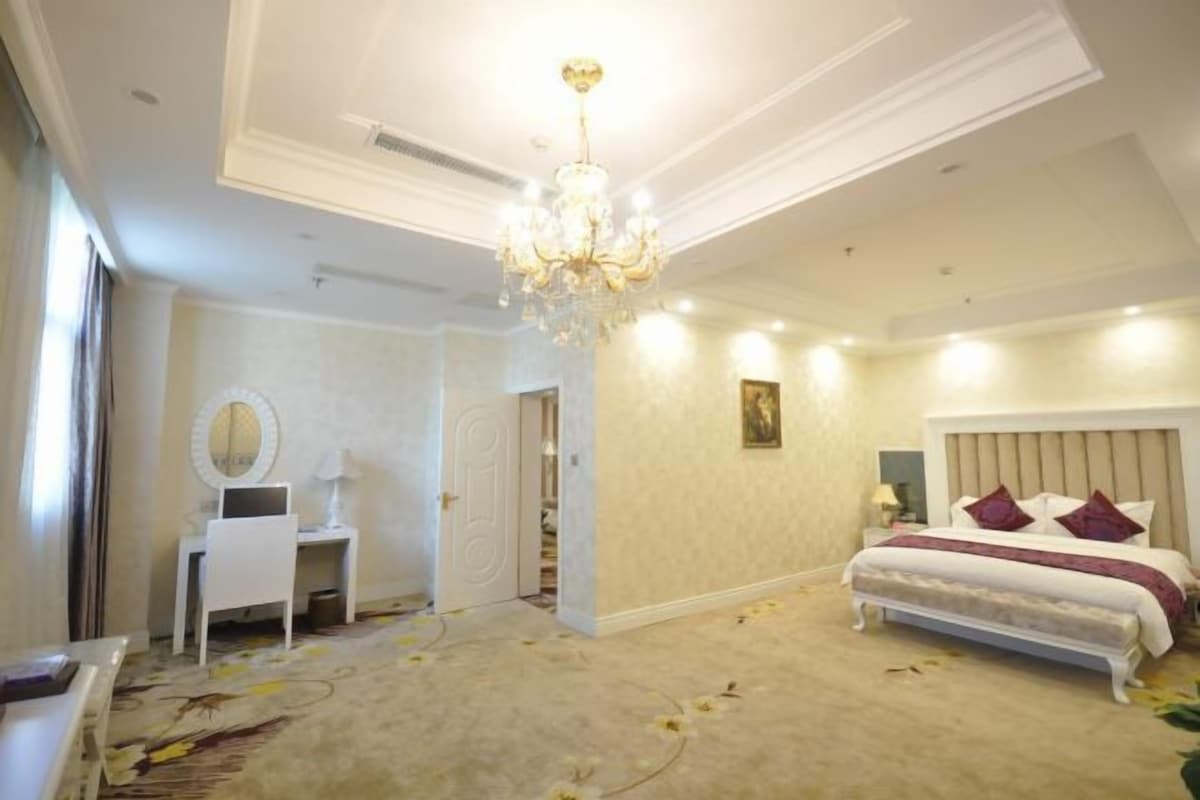 A bedroom with a bed, a desk, a mirror, and a chandelier.