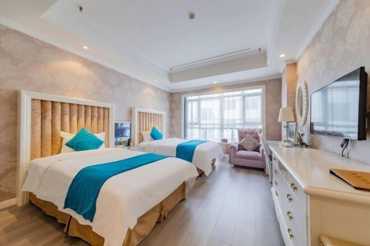 A hotel room with two beds, a TV, a desk, and a window.