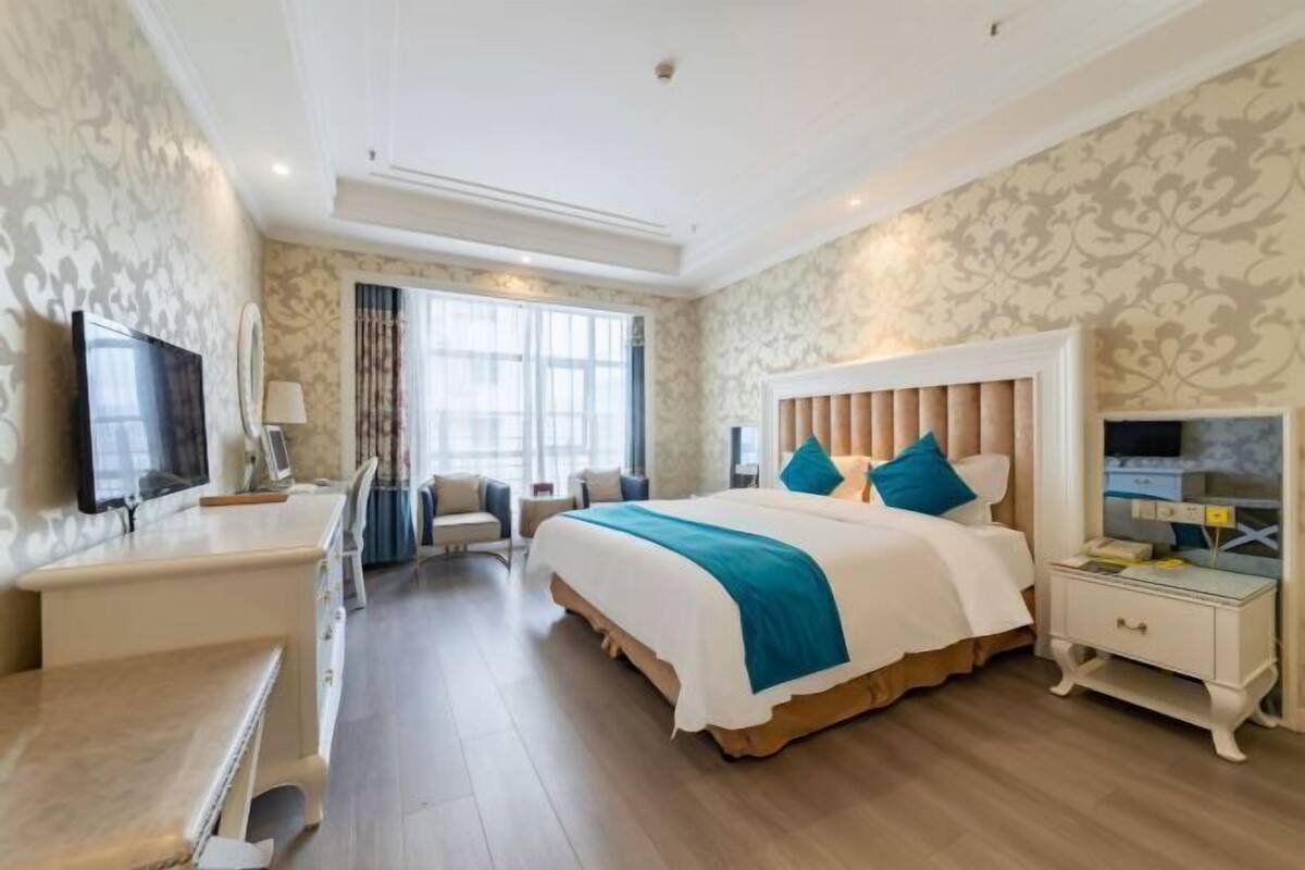 A hotel room with a bed, bedside table, TV, and a desk with a chair.