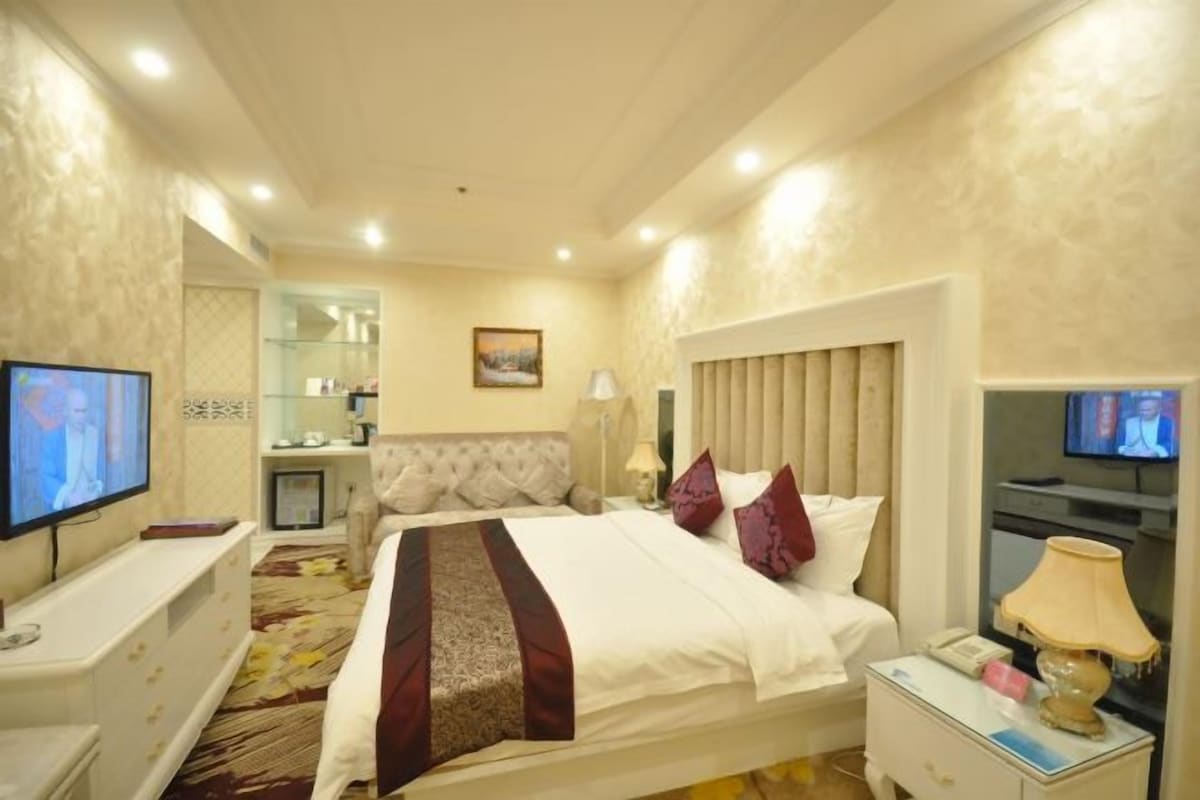 A hotel room with a bed, bedside table, TV, and a mirror.