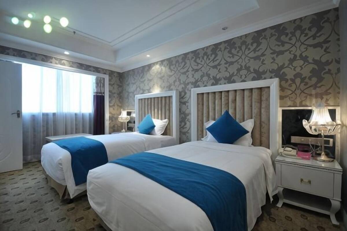 A hotel room with two beds, a nightstand, a lamp, and a door leading to a balcony.